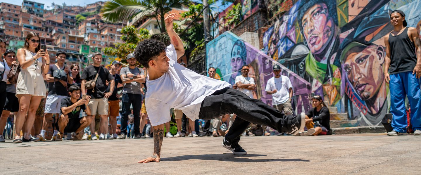 Breakdancer performing in Comuna 13 plaza surrounded by murals and spectators